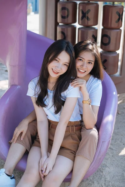 公園で一緒に遊び場のスライダーの端に座って白いTシャツの2人の女の子笑顔で — ストック写真