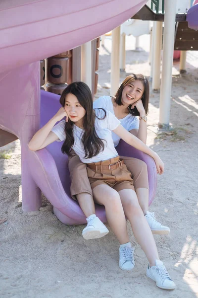 Dwie Dziewczyny Białej Koszulce Siedzące Końcu Suwaka Placu Zabaw Razem — Zdjęcie stockowe