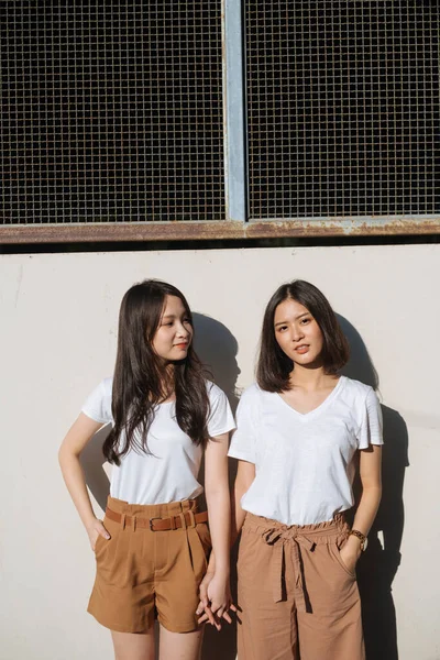 Dvě Dívky Bílém Tričku Hnědých Kalhotách Stojící Slunci Zdi Drží — Stock fotografie