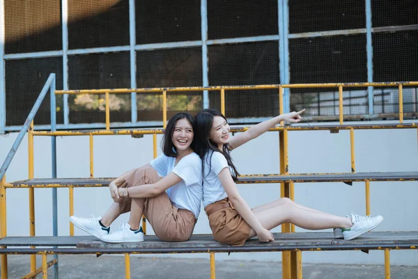 Dwie Dziewczyny Białej Koszulce Brązowe Spodnie Siedzące Plecami Siebie Uśmiechające — Zdjęcie stockowe