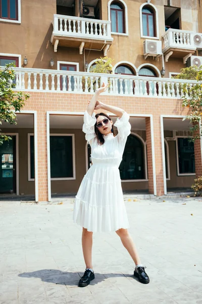 美丽的长发姑娘 穿着白色的衣服 站在棕色大楼前面的阳光下 姿势华丽极了 — 图库照片