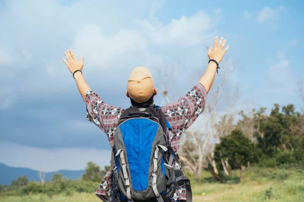 Male adventurer raise his hands to the bue sky like he's happy.