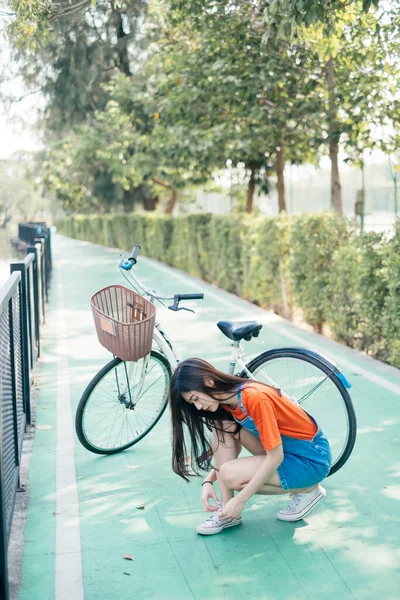 Long hair girl in orange t-shirt and jeans jumper sit on the floor and tie her shoelace in bicycle lane.