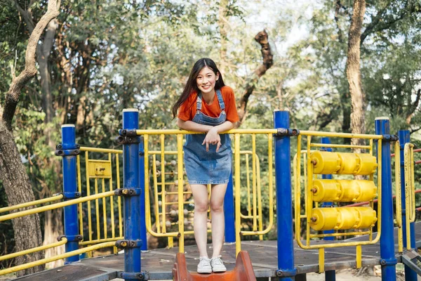 Long hair girl in orange t-shirt and jeans jumper standing on the top of playground slider.