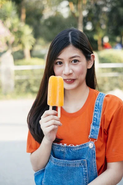Long hair girl in orange t-shirt and jeans jumper show the orange ice cream.