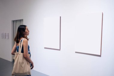 Güzel genç Asyalı kadın sanat galerisindeki boş kağıt tuvale bakıyor..