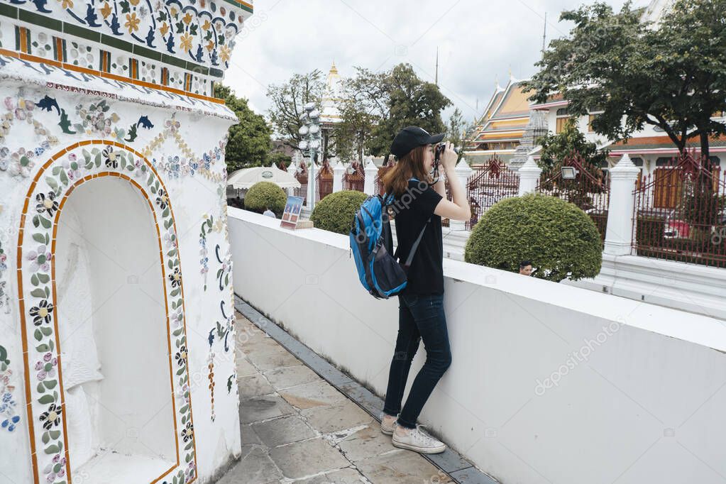 Side view of asian backpacker woman taking picture with camera at wat arun.