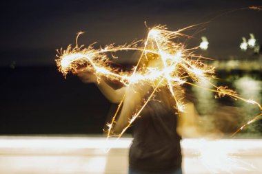 Bir kadın gece maytap kullanarak bir yıldız şekli çiziyor. Uzun pozlama. Sahilde..