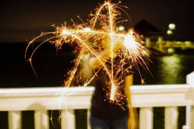 Bir kadın gece maytap kullanarak bir yıldız şekli çiziyor. Uzun pozlama. Sahilde..