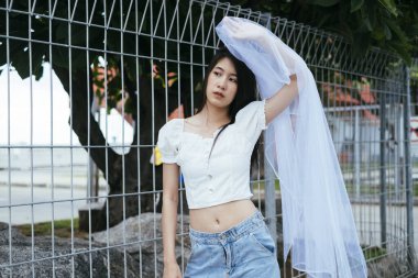 Sokaklarda beyaz peçeli, Asyalı, genç, uzun, siyah saçlı bir gelinin portresi. Moda portresi.