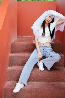 Hipster genç Asyalı, uzun siyah saçlı, beyaz peçeli bir gelin açık merdivenlerde oturuyor. Bangsaen Tayland.