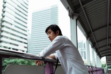 Üzücü genç Taylandlı işadamı üst geçitte duruyor, ellerini tırabzanlara dayayıp yola bakıyor. İşten ayrıldıktan sonra stresli Tayland işi.