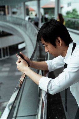 Şehirdeki tırabzanlar üzerinde cep telefonu kullanan Asyalı iş adamı..