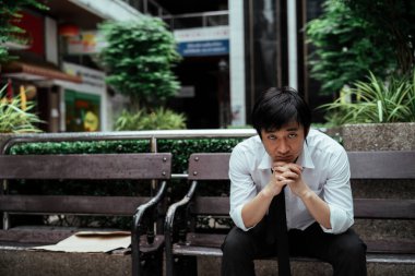 Tuhaf görünüşlü Asyalı işadamı bankta oturmuş kameraya bakıyor..