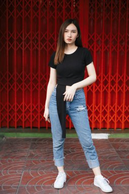 Tam boy moda portresi - Güzel hippi Asyalı siyah gömlekli ve kot pantolonlu kadın kırmızı mekik kapısının üzerinde.