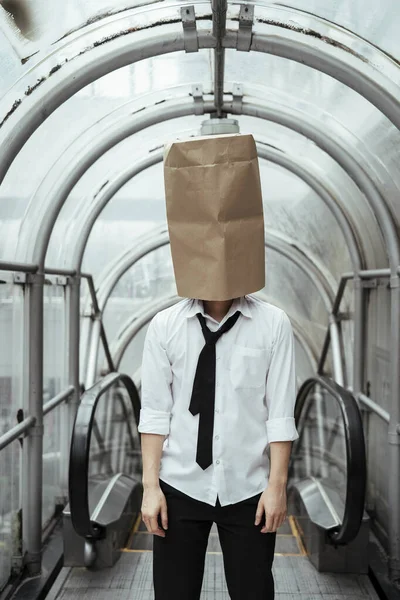 Businessman with a cardboard bag on his head. Businessman covering his head with paper bag in city tunnel.