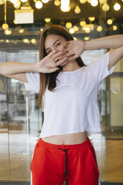 Fashion portrait - Beautiful asian young woman in white shirt and red sport pant posing over beautiful yellow bokeh at background.