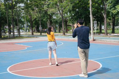 Erkek fotoğrafçı, kız modelin basketbol sahasında dururken, zıplarken ve otururken fotoğrafını çeker..