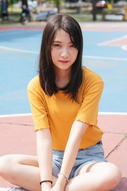 Güneşli bir günde esmer kız ayakta, atlıyor ve basketbol sahasında oturuyor..