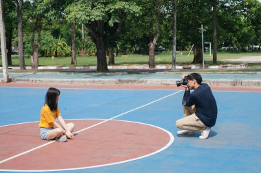 Erkek fotoğrafçı, kız modelin basketbol sahasında dururken, zıplarken ve otururken fotoğrafını çeker..