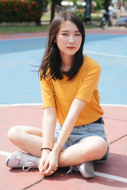 Güneşli bir günde esmer kız ayakta, atlıyor ve basketbol sahasında oturuyor..