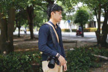 Kameraman elinde kamerasıyla parkta dikilirken çekimlere ara veriyor..
