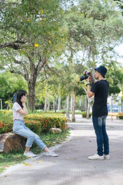 Erkek fotoğrafçı, ixora çalılığında kayanın üzerinde oturan manken kızın fotoğrafını çekiyor..