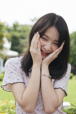 Utangaç uzun saçlı kız ixora çalılığında otururken yüzüne dokunuyor..