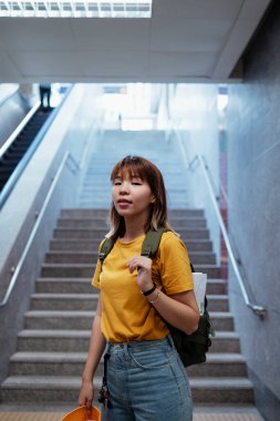 Yeşil sırt çantalı sarı sırt çantalı kadın metro istasyonunda merdivenin sonunda duruyor..