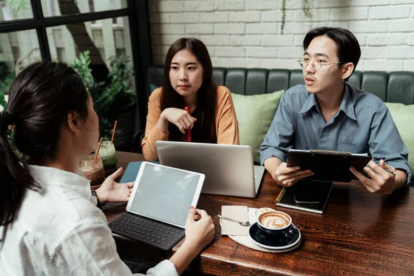 Young startup business people discussing about the plan before invest in something. Young business people talking about the idea of project to their work mate in cafe. Business people metting corporate communication. Three young asian business workin