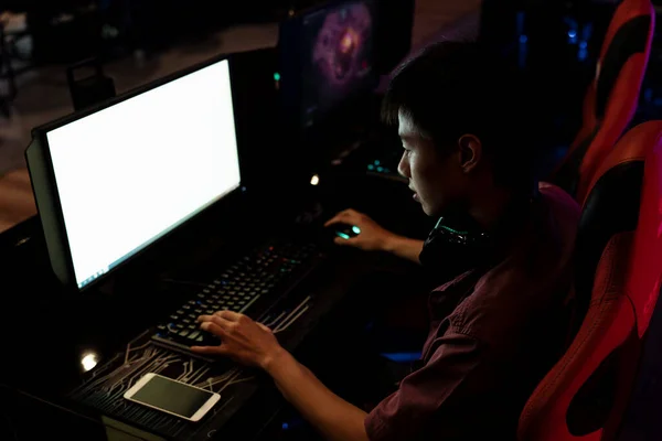 White screen on monitor at internet cafe. Asian gamer playing game on PC, sitting on a red chair. Game addicted. Copy space.