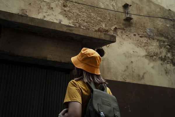 Żółty Backpacker Kobieta Zielonym Plecakiem Stoi Patrząc Stary Zardzewiały Dom — Zdjęcie stockowe