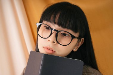 Uzun siyah saçlı güzel Asyalı kadın siyah bir kitapla gözlük takıyor. İş kadınının moda portresi. Telefondan çalış.