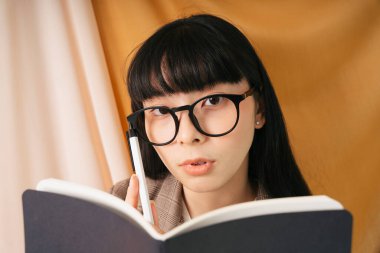 Yakından - güzel Asyalı Taylandlı uzun siyah saçlı gözlüklü kadın kitap okuyor. Güzel inek kadın bir kitaba not alıyor..