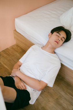 Siyah saçlı adam yatağın yanına oturur, başını yatağa dayar ve gözlerini kapatır. Garip bir uyku pozisyonu..