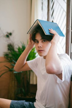 Kısa saçlı, sıradan görünüşlü bir adam. Kitabı kafasının üzerine, pencereye bırak..