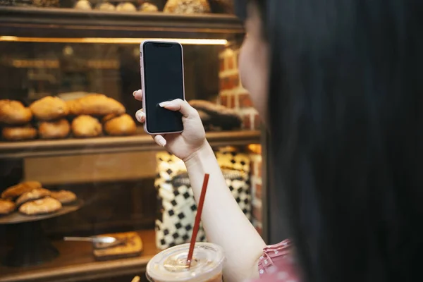 Beautiful asian thai long dark hair woman taking picture of bread inside bakery shop from window street outdoor. Travel and eat concept.