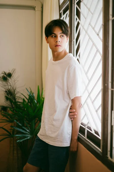 Cool and handsome guy stand at the window with fence, look outside the window.