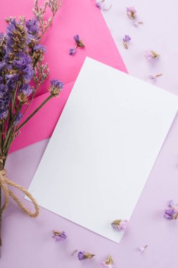 Mor çiçekli beyaz kağıdı pastel pembe arka planda taklit et. Üst görünüm.
