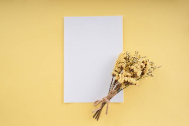 Parlak arkaplandaki sarı çiçekli beyaz kağıdı taklit et. Üst görünüm.