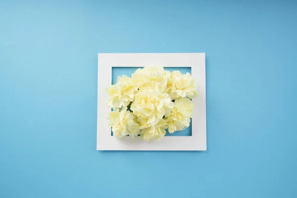Mock up white frame with yellow flower over bright blue background. Top view. Copy space.