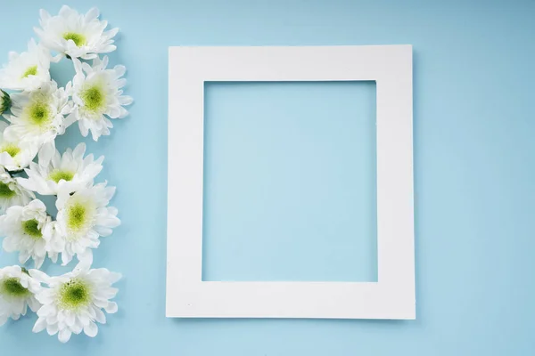 Mock up white frame with flower over bright blue background. Blooming season concept.