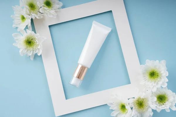 Cream lotion natural product bottle inside white frame background with flower over blue background.