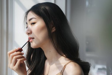 Dalgalı uzun saçlı kız pencerenin yanında dururken ruj sür..