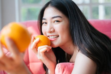 Canlı, uzun saçlı kız pembe kanepeye uzanmış portakalları parlak bir gülümsemeyle elinde tutuyordu..