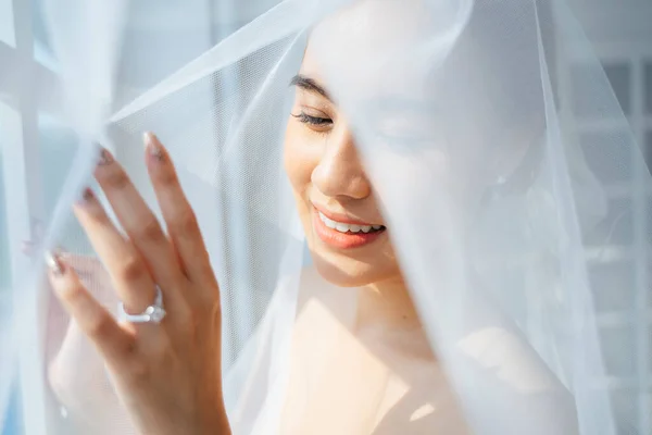 Pony tail blond hair woman finish dress up in the morning of her wedding day, standing nex to the window, cover herself with white veil and touch the window to show her wedding ring.