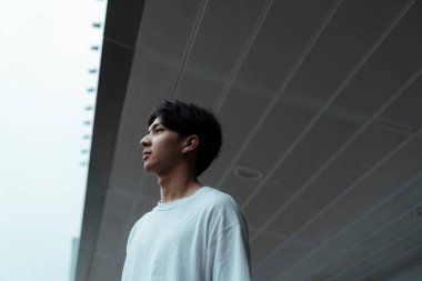 Alışveriş merkezinin tentesinde duran beyaz tişörtlü adam, çevresine bak..