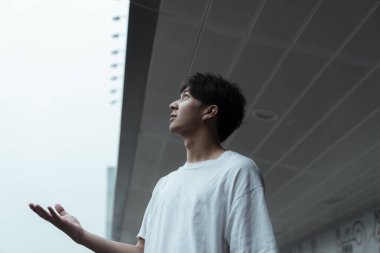 Genç adam binanın önünde duruyor ve yüzü gökyüzüne bakıyor..