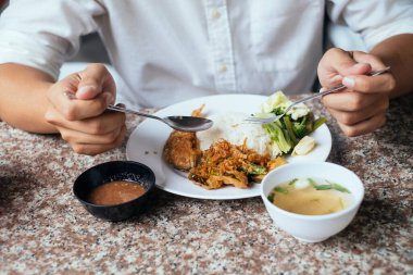 Yemek saatinde elinde çatal ve kaşıkla beyaz gömlekli adamın önündeki masada kesilmiş yemek görüntüsü..