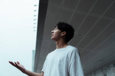 Genç adam binanın önünde duruyor ve yüzü gökyüzüne bakıyor..